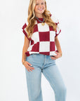 Front-facing Checkmate Burgundy Sweater Vest paired with light denim jeans, showcasing its cozy knit texture and fall-ready checker design.