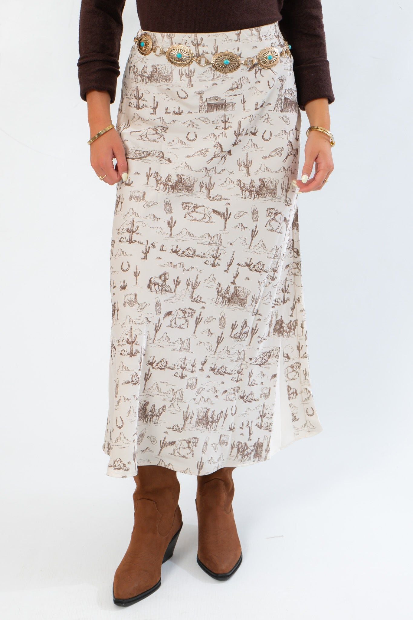 Close-up of Old West Satin Maxi Skirt featuring detailed brown western icon patterns on cream satin, styled with a turquoise concho belt and boots.