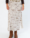 Close-up of Old West Satin Maxi Skirt featuring detailed brown western icon patterns on cream satin, styled with a turquoise concho belt and boots.