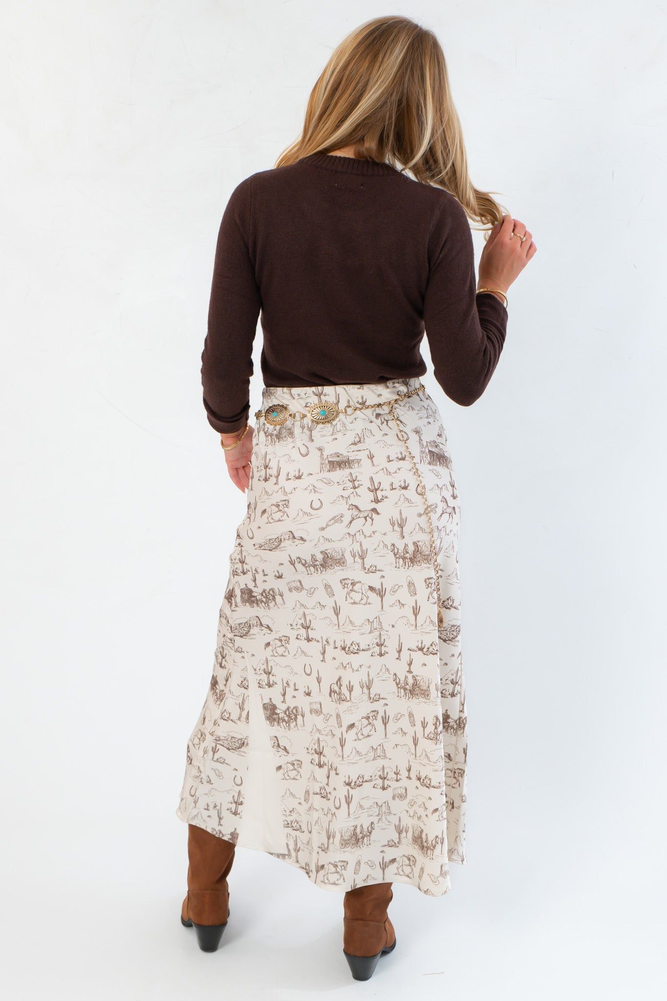 Back view of Old West Satin Maxi Skirt showing western icon print and elegant drape, styled with a dark sweater and heeled boots for a chic western vibe.