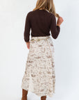 Back view of Old West Satin Maxi Skirt showing western icon print and elegant drape, styled with a dark sweater and heeled boots for a chic western vibe.