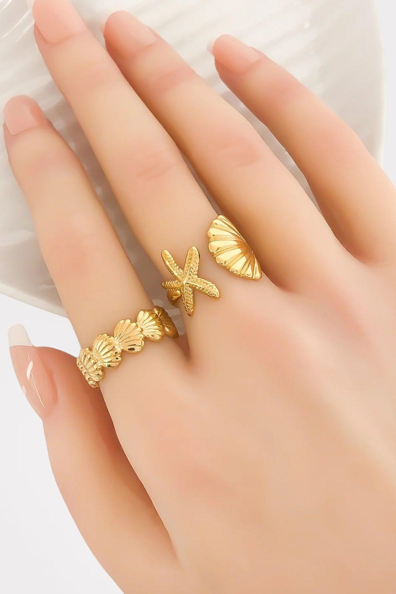 Elegant gold-plated seashell and starfish ring worn on a hand. Adjustable and water-resistant, ideal for ocean-inspired fashion and summer accessories.