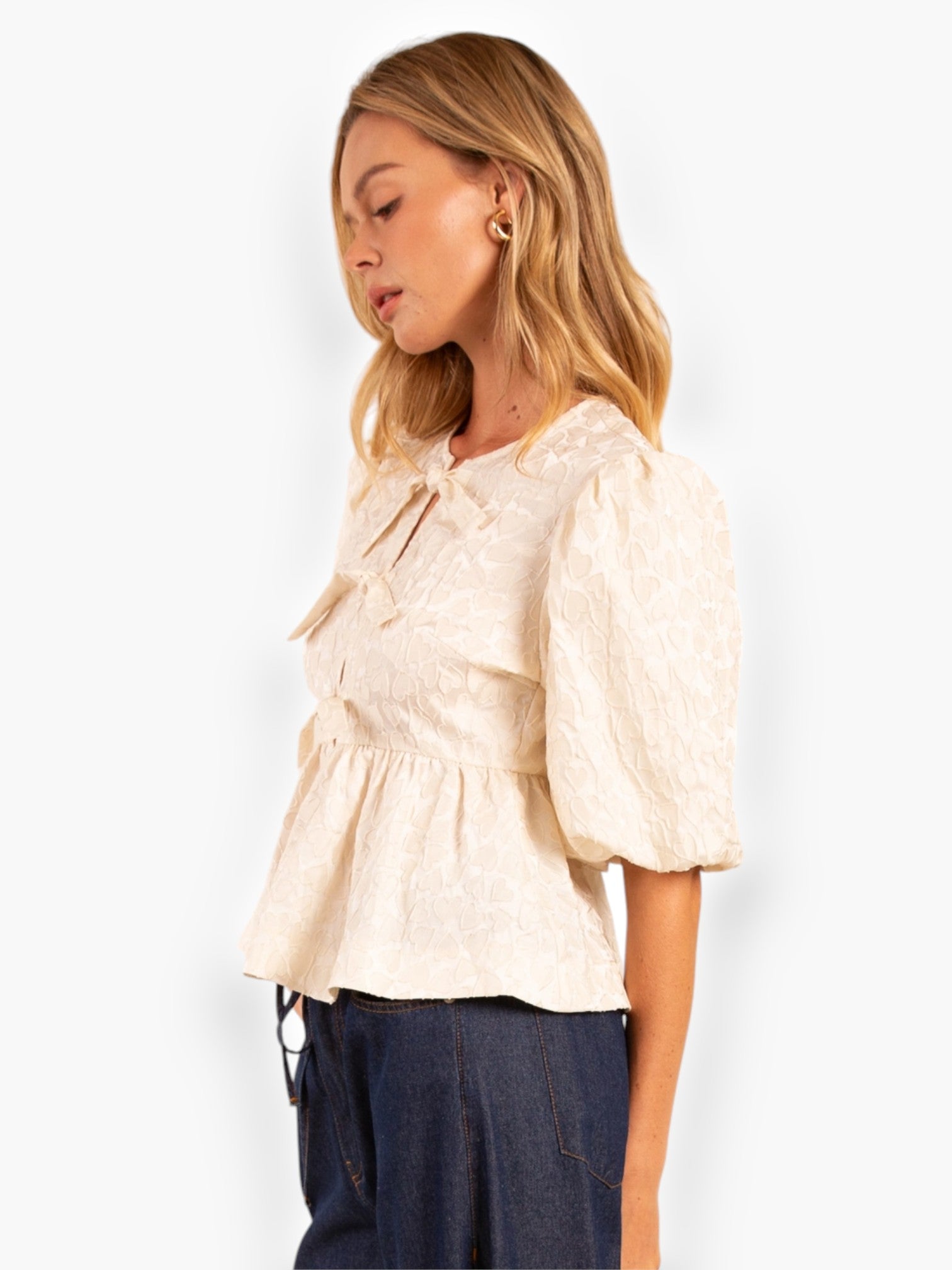 Side profile of Heart Texture Cream Peplum Top featuring puffed sleeves and bow details, ideal for a stylish and romantic outfit.