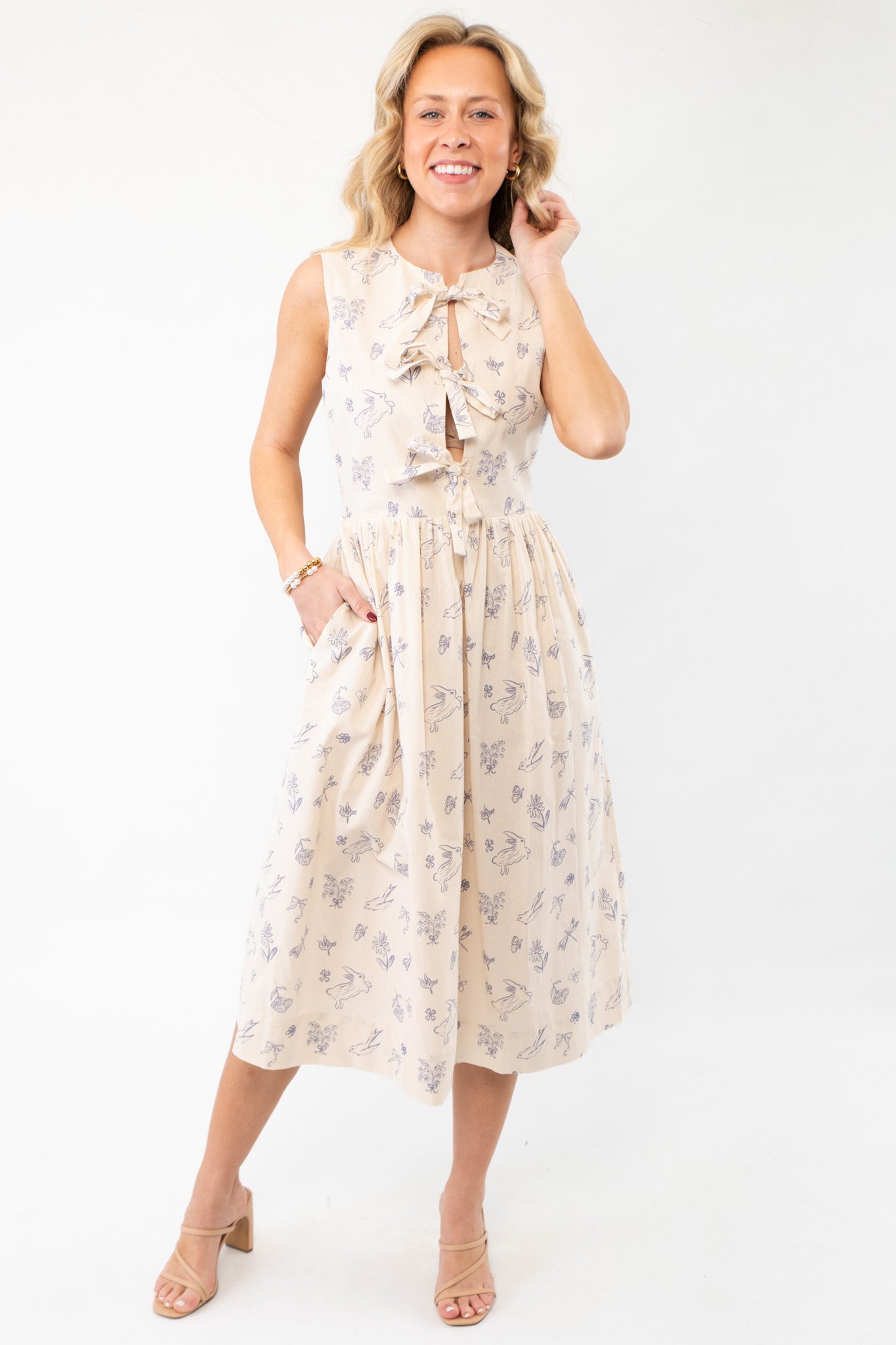 Model wearing the Hop To It Beige Bunny Pattern Midi Dress, showcasing its whimsical Easter charm, side pockets, and elegant midi length.