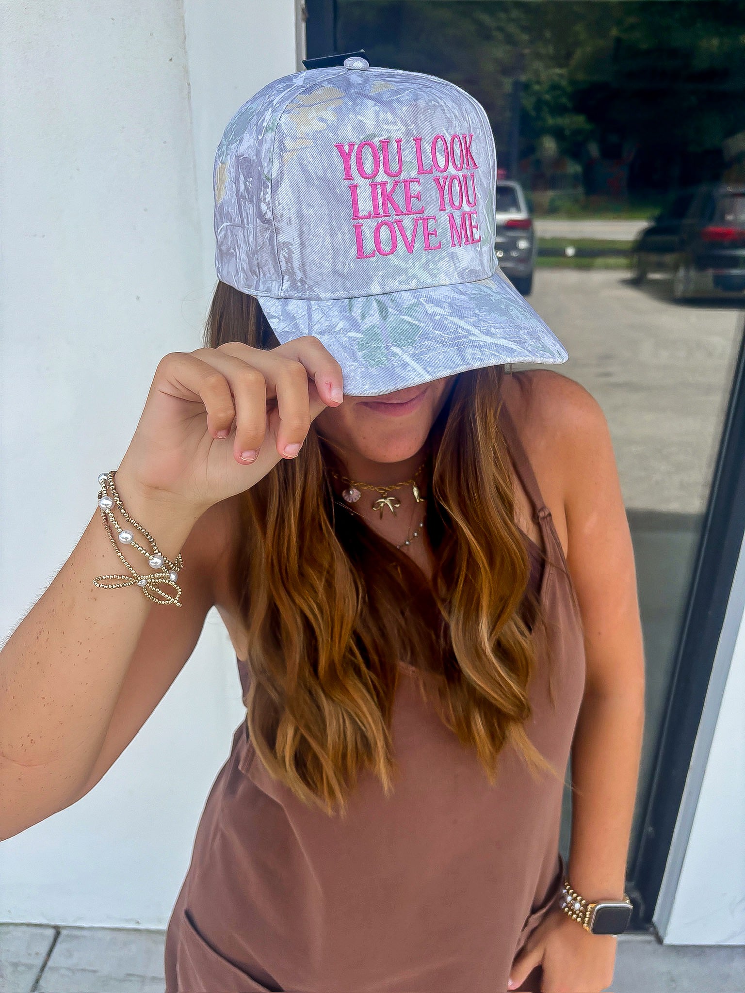 Trendy You Look Like You Love Me Camo Trucker Hat styled with casual outfit, showcasing pink embroidered lyrics and western-inspired design.