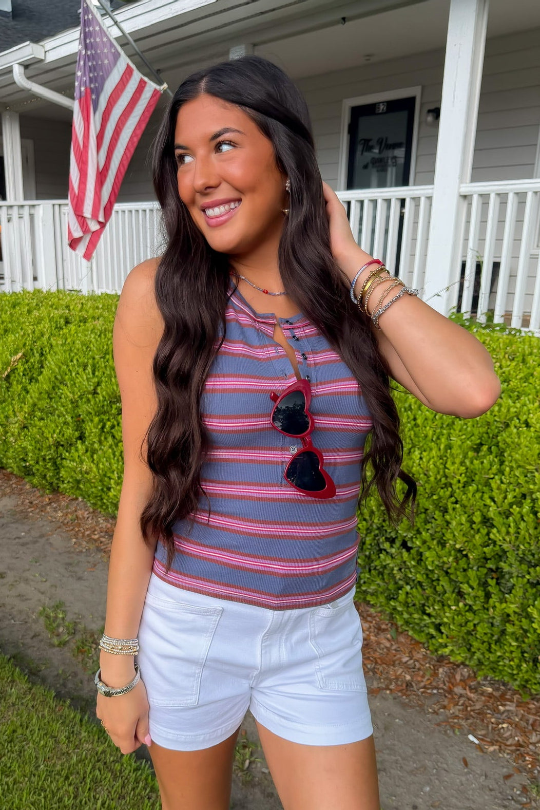 Woman in striped tank top and shorts standing in front of a house with an American flag.