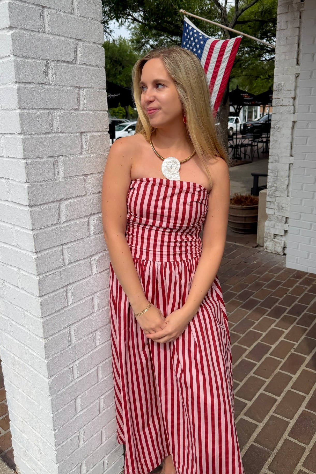 Woman in a red and white striped dress standing next to a white brick wall with an American flag in the background.