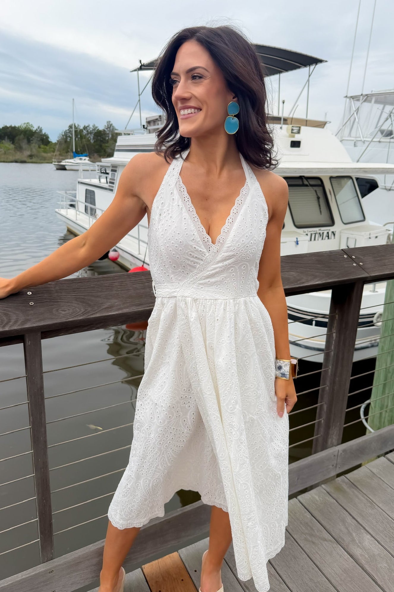 Woman in a white dress standing on a dock with boats in the background