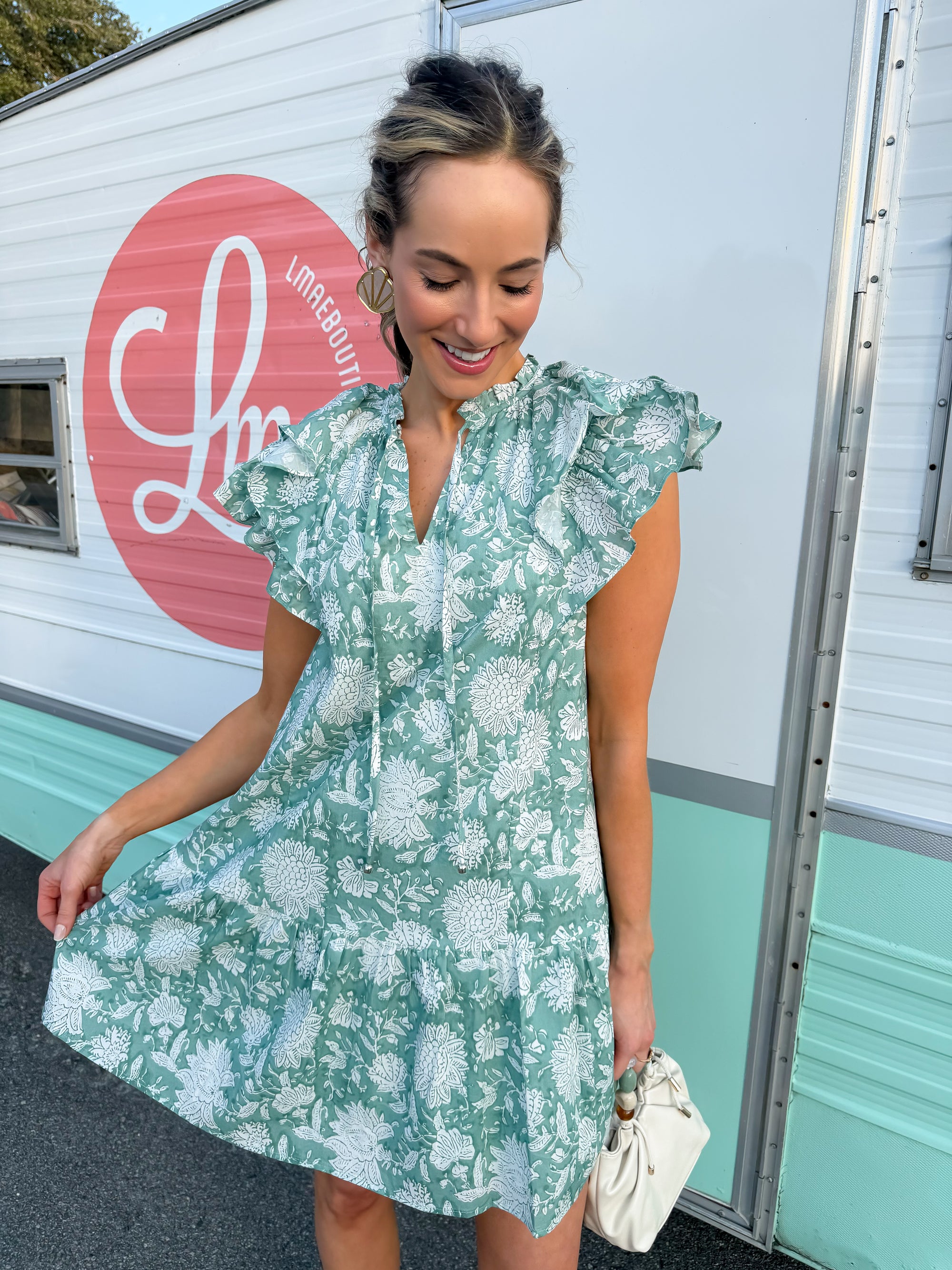 Woman in a green floral dress standing in front of a building with a pink logo in Litchfield Beach