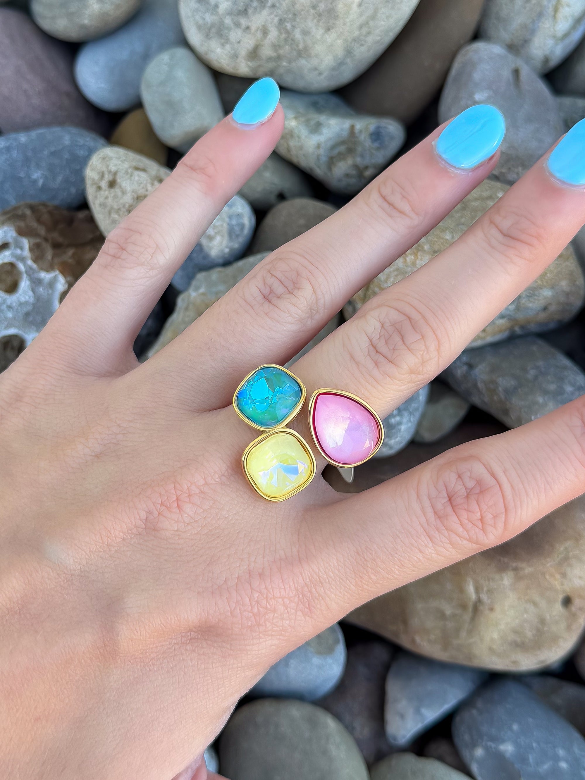 Close-up of Aurora Gemstone Ring with three vibrant stones—blue, yellow, and pink—set in a gold-tone adjustable open band, worn on hand.