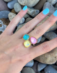 Close-up of Aurora Gemstone Ring with three vibrant stones—blue, yellow, and pink—set in a gold-tone adjustable open band, worn on hand.
