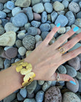 Golden Monarch Cuff Bracelet with butterfly design in polished gold finish, worn on wrist over smooth river stones. Adjustable and stackable jewelry.