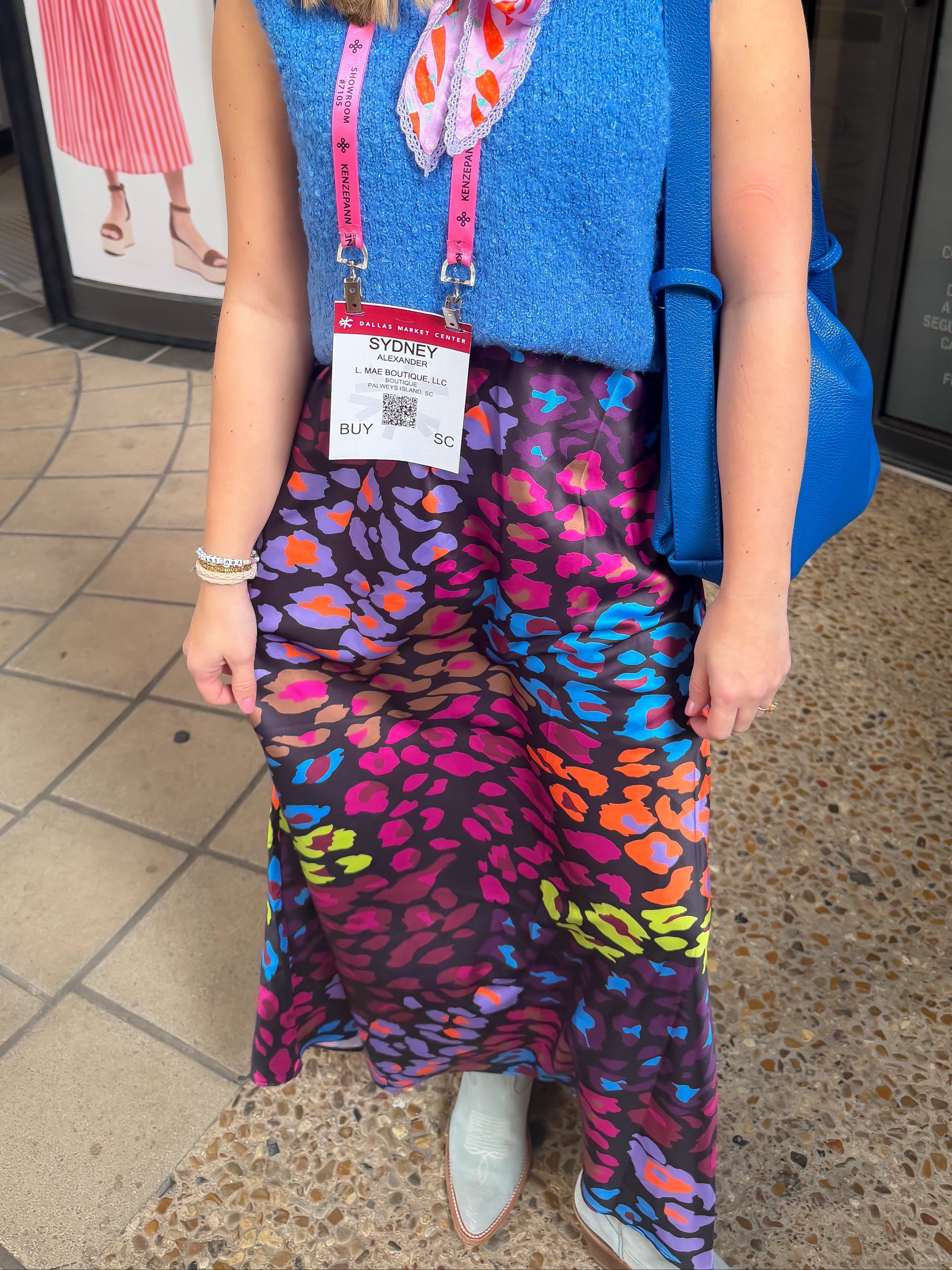 Woman wearing a blue sleeveless top and colorful leopard print skirt standing on a tiled floor.