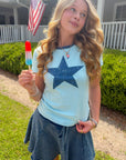 Girl holding a red, white, and blue popsicle  in a baby blue star t shirt in front of a house with an American flag.