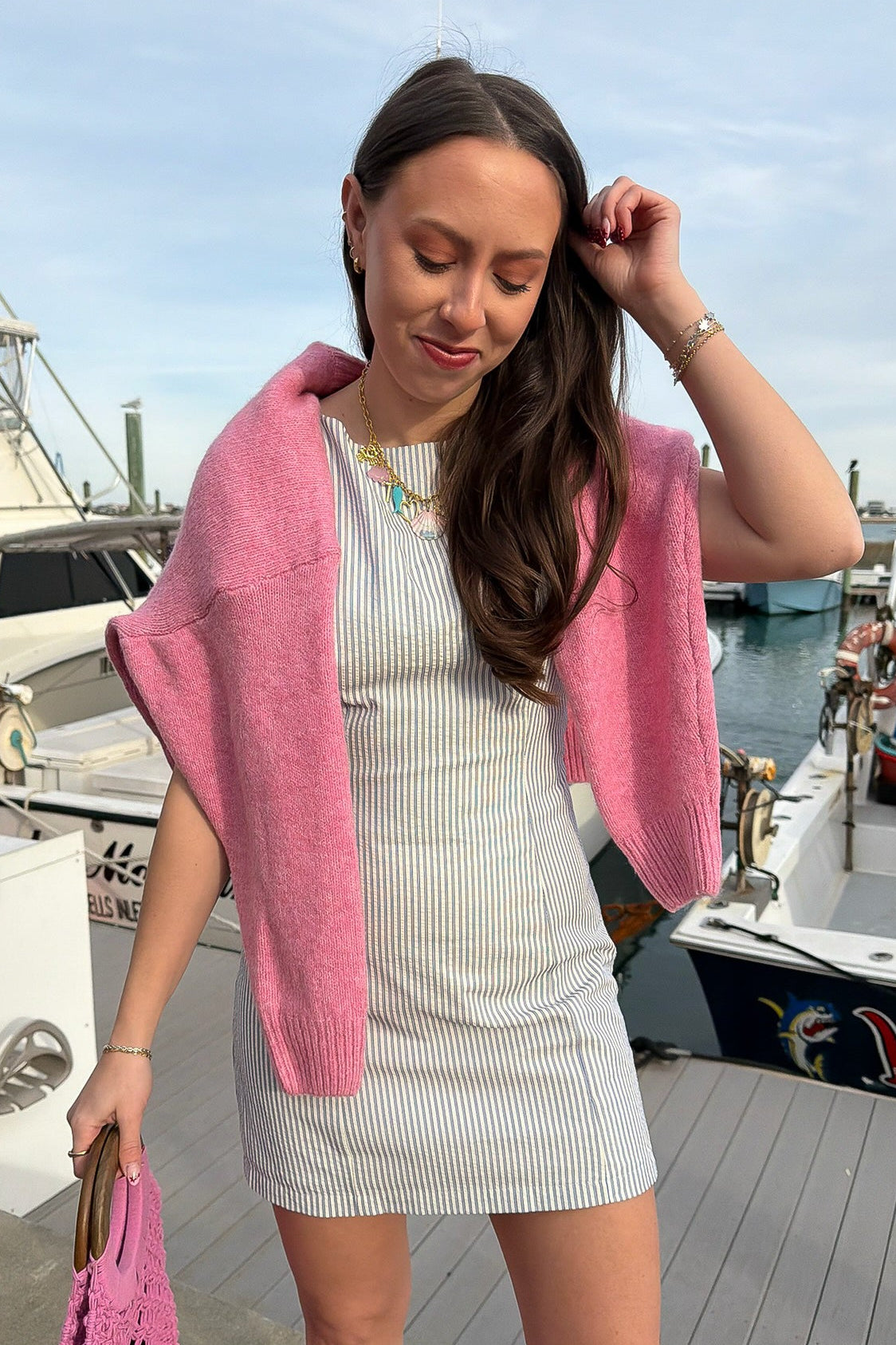 Woman in a white dress with a pink cardigan standing on a dock with boats in the background