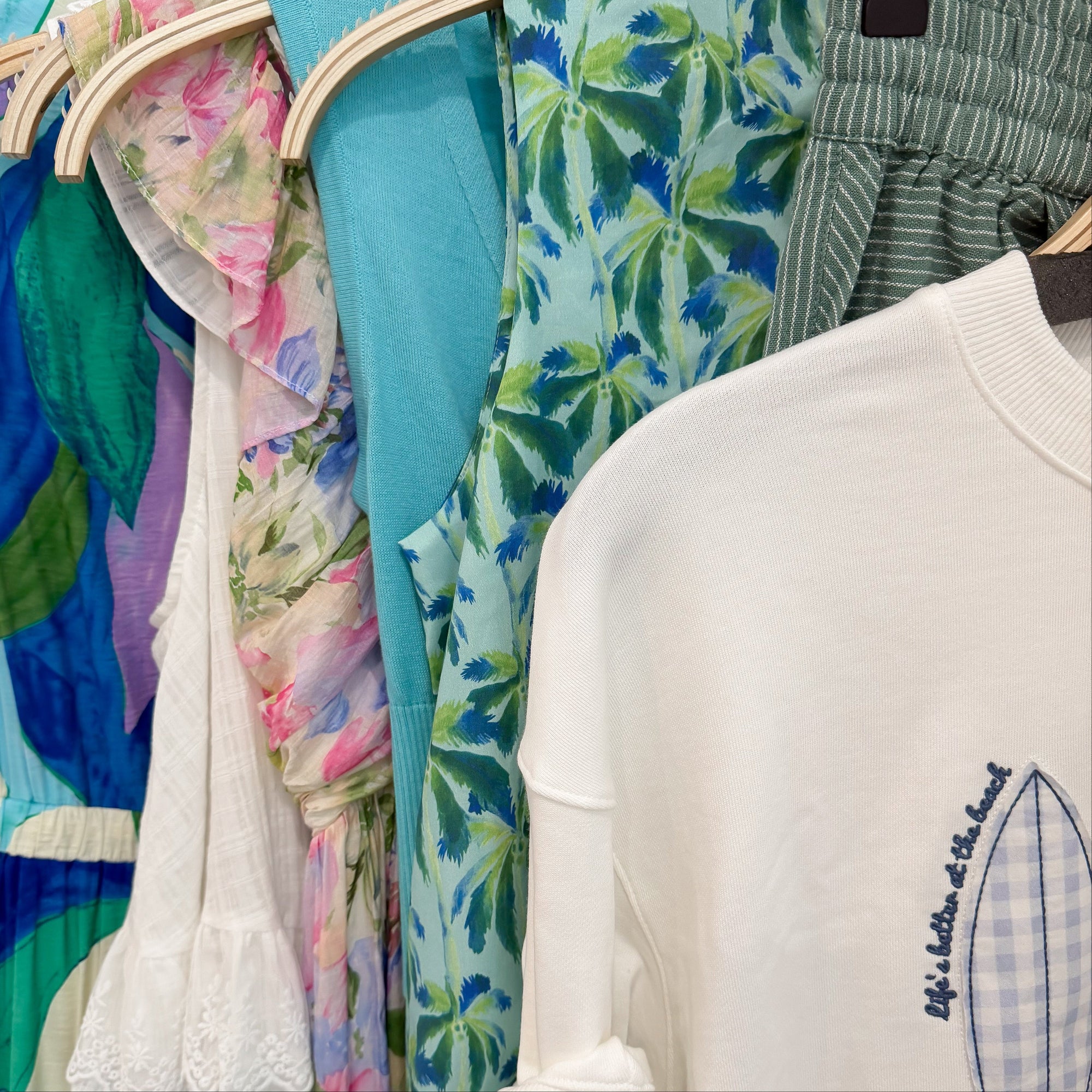 Colorful clothing on hangers with a focus on a white sweater with a blue graphic.
