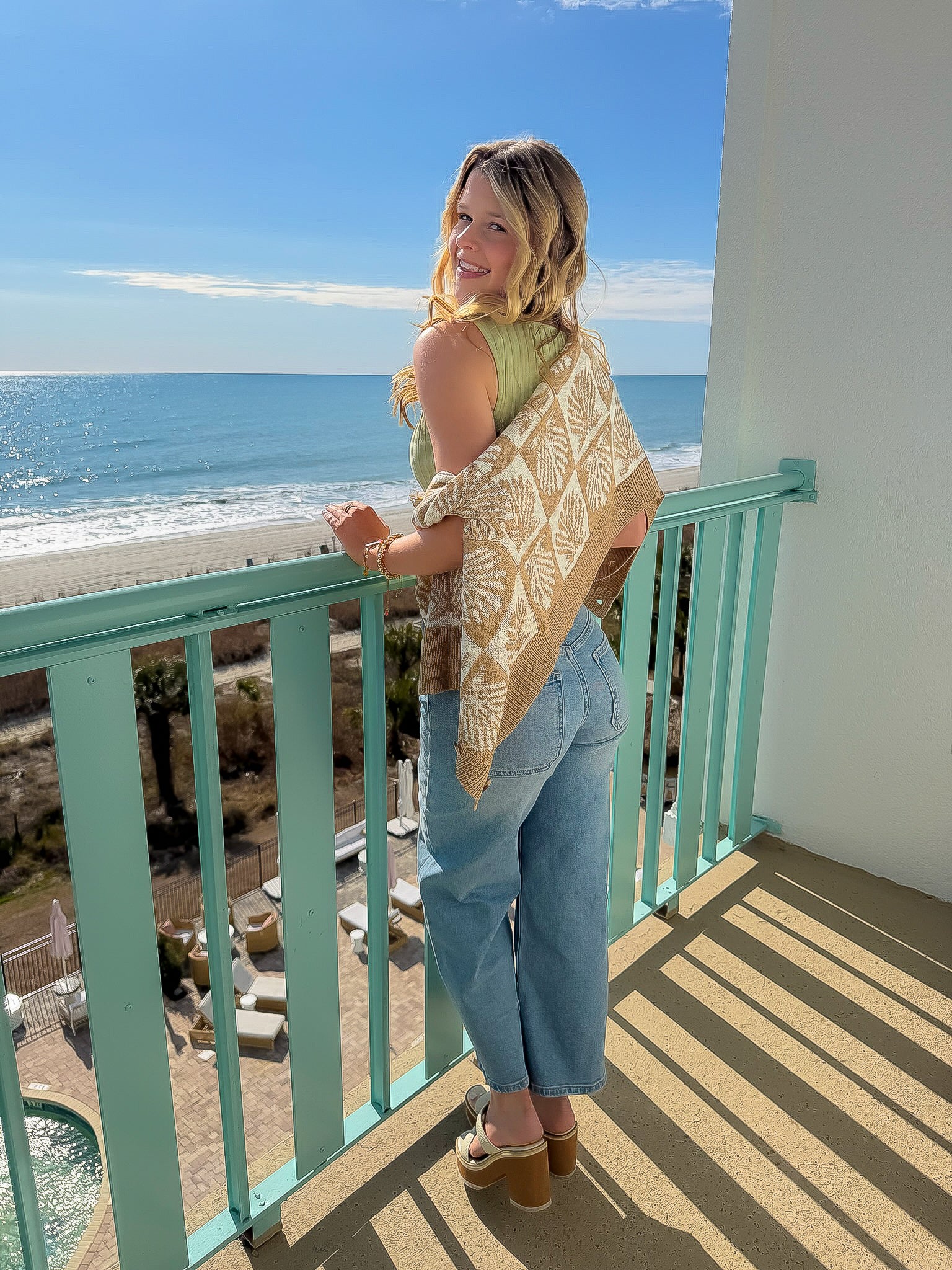 Cowrie Cutie Seashell Cardigan draped over shoulders in a beachside setting, styled with jeans for a relaxed coastal look.