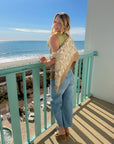 Cowrie Cutie Seashell Cardigan draped over shoulders in a beachside setting, styled with jeans for a relaxed coastal look.
