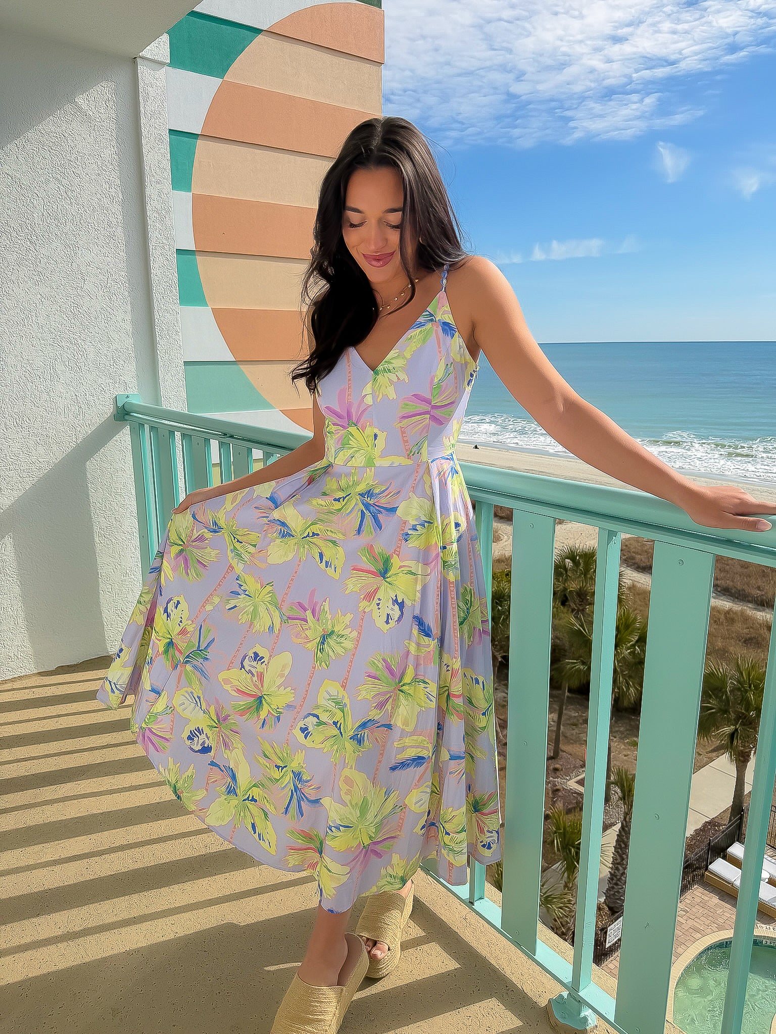 Woman in a colorful dress standing on a balcony with a scenic ocean view.