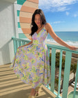 Woman in a colorful dress standing on a balcony with a scenic ocean view.
