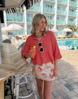 Sally Red Seashell Printed Mini Skirt styled with a coral knit top at a poolside bar. Coastal-chic poppy red shell print perfect for summer getaways.