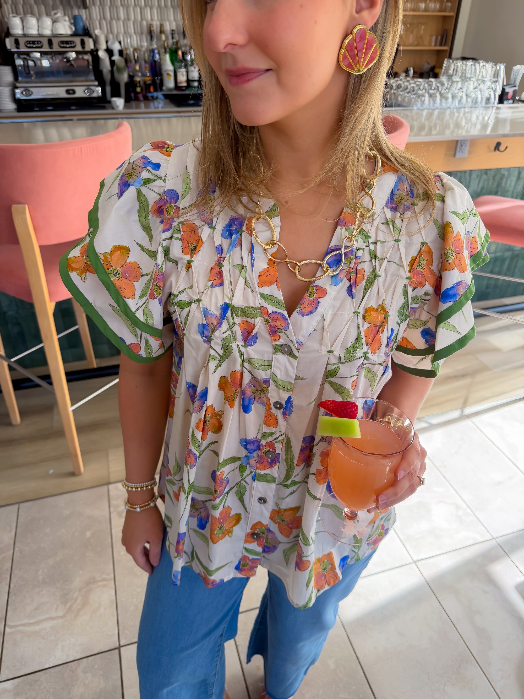 Front view of Spring Fling Floral Ruffle Sleeve Blouse featuring pleated details and vibrant floral pattern, styled with gold jewelry and a cocktail.