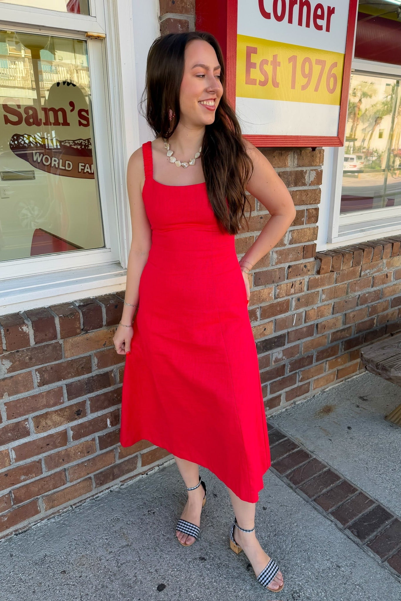 Woman in a red dress standing outside a store with a brick wall and sign in the background.