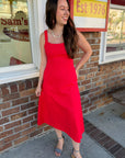 Woman in a red dress standing outside a store with a brick wall and sign in the background.