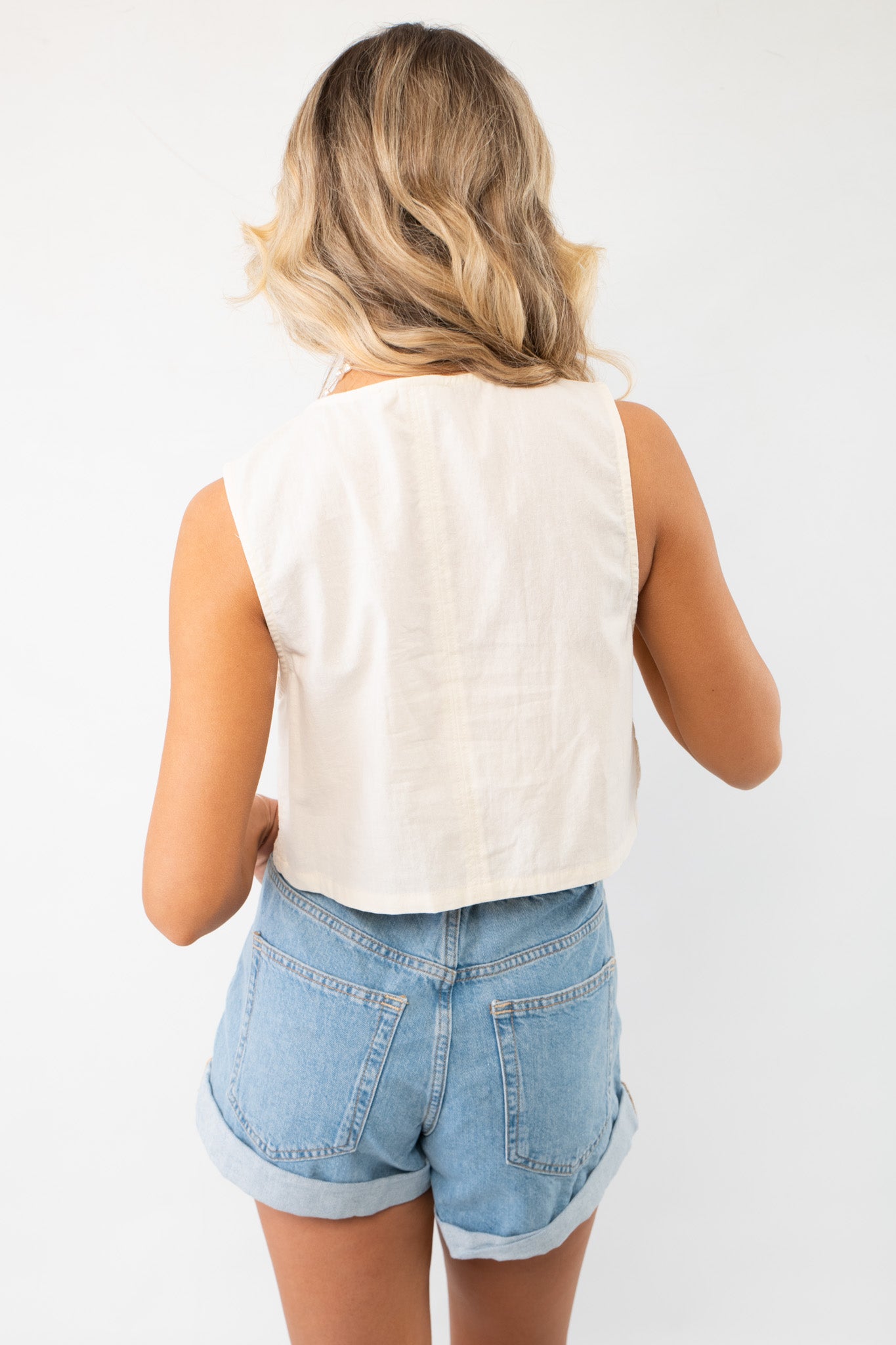 Back view of the Jolene Beige Embroidered Tie Top Vest, showcasing its solid beige fabric and cropped cut, ideal for layering over casual outfits.