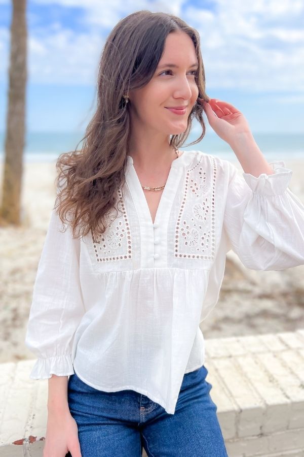 Chic and feminine Natalie White Eyelet Button Blouse with a relaxed fit, eyelet embroidery, and ruffled cuffs. A must-have for effortless spring fashion.