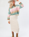 Woman wearing a colorful striped sweater, cream skirt, and cowboy boots on a white background
