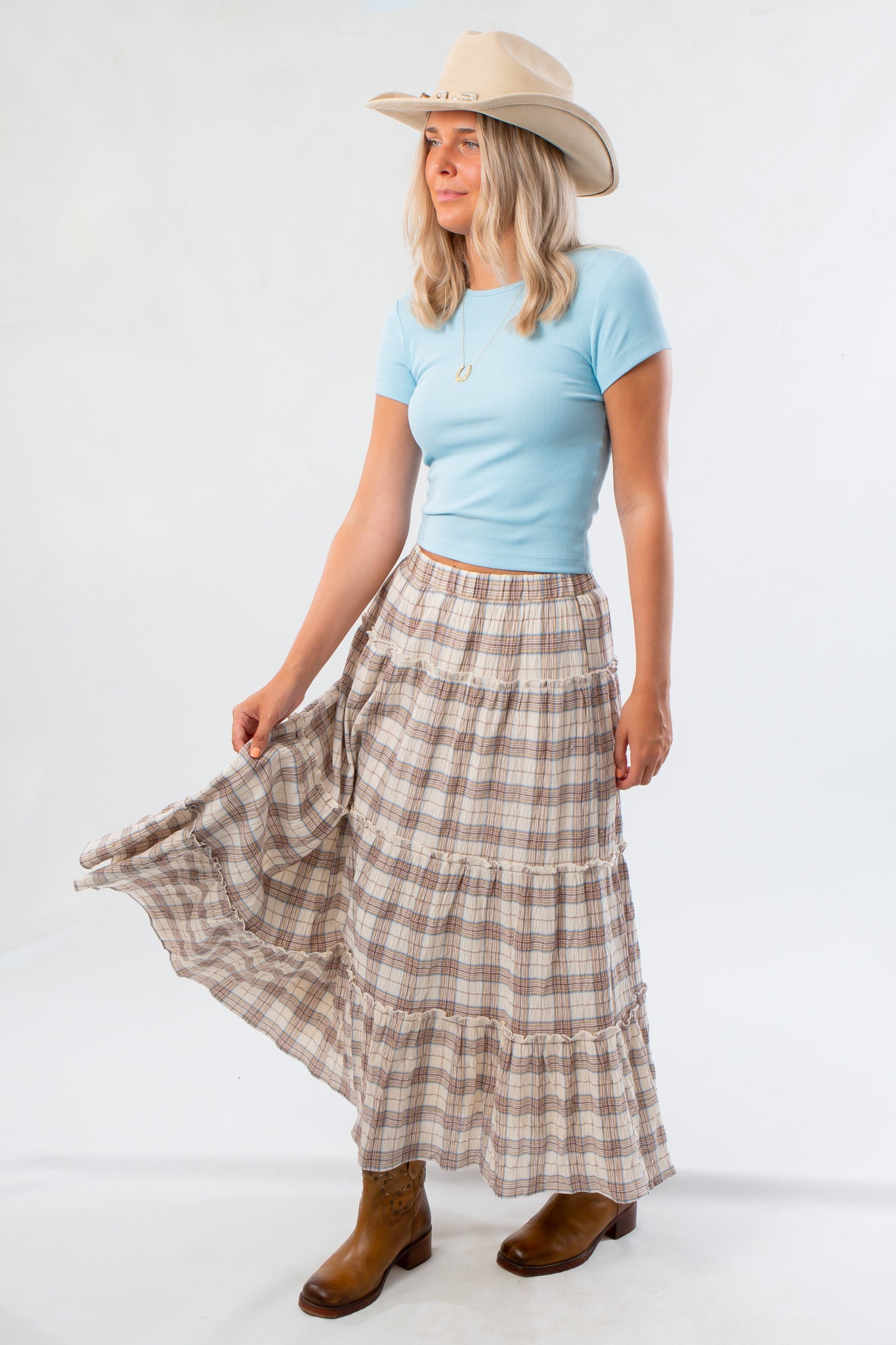 Side view of Brown Plaid Maxi Skirt - Fort Worth paired with a blue tee and boots, highlighting its flowing tiered silhouette.