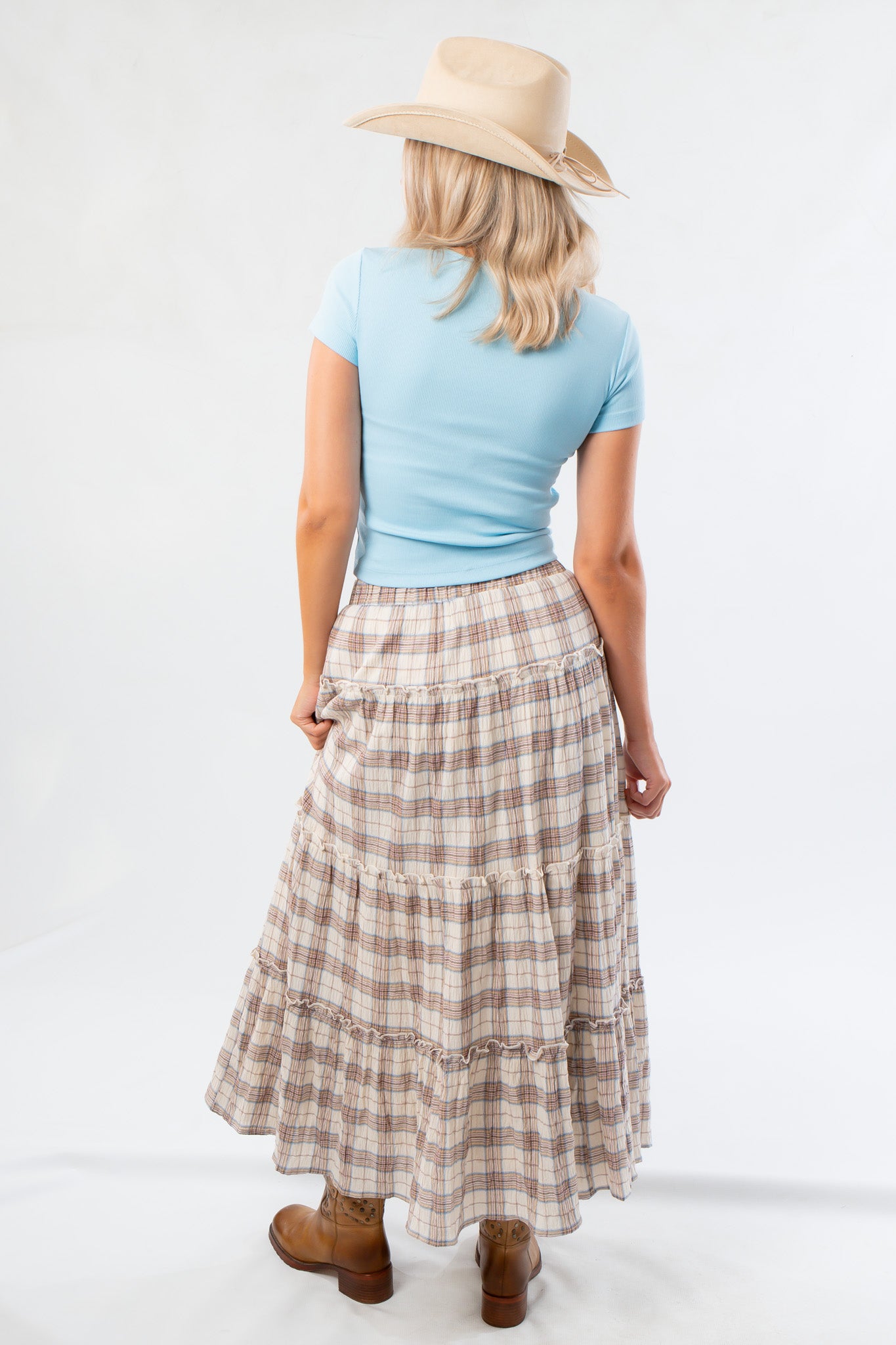 Back view of Brown Plaid Maxi Skirt - Fort Worth showing tiered layers and elastic waistband, styled with a blue tee and hat.