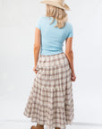 Back view of Brown Plaid Maxi Skirt - Fort Worth showing tiered layers and elastic waistband, styled with a blue tee and hat.