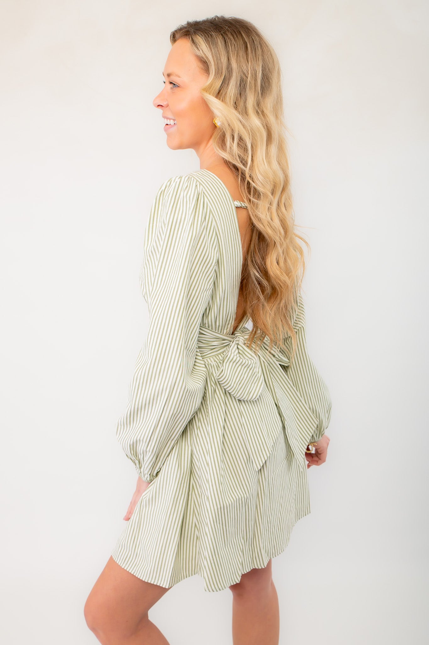 Side view of sage striped open back mini dress with a bow tie detail, showcasing its flattering silhouette and breezy resort-ready style.