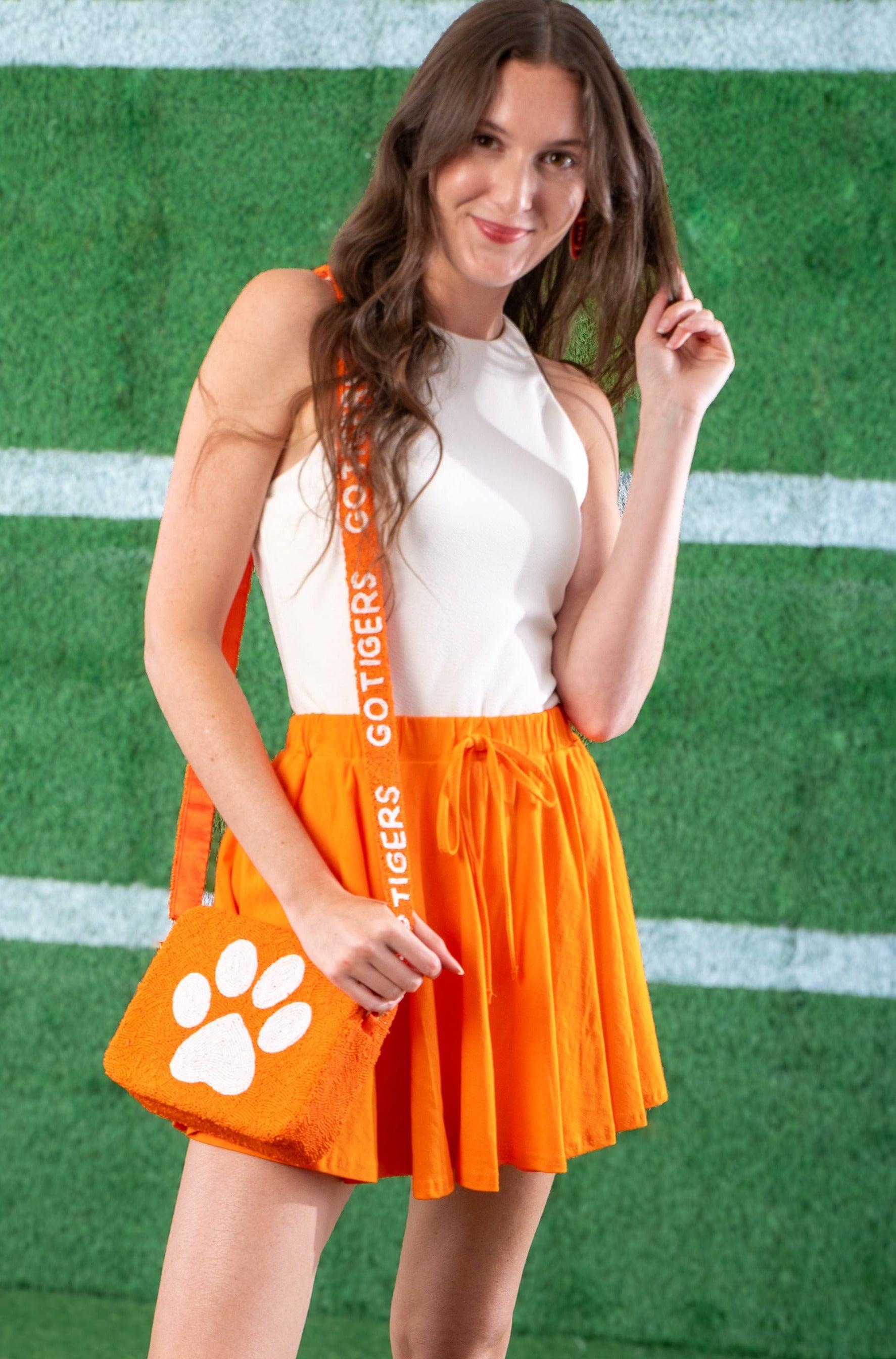 Bright orange flowy skort styled with a white top and matching accessories. Ideal for game day with built-in shorts and a comfortable fit.