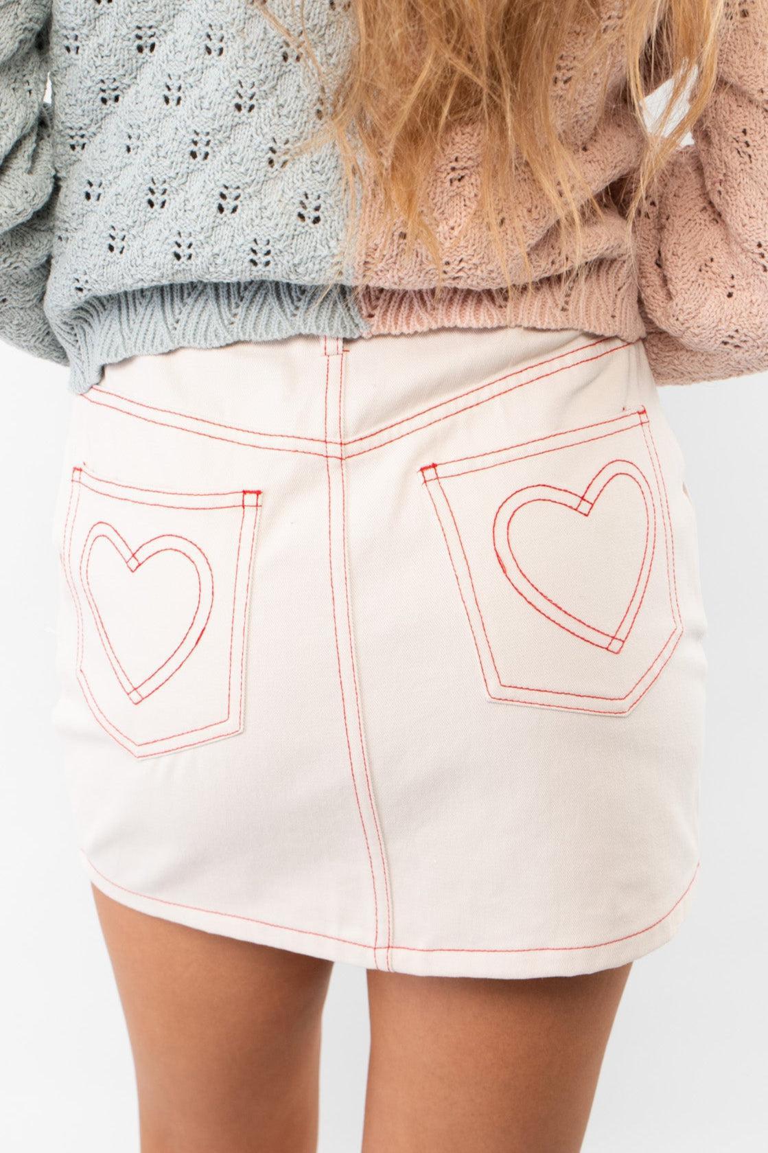 Stitched With Love Pink Denim Heart Skirt featuring red heart stitching on back pockets. A playful and chic mini skirt perfect for trendy outfits.