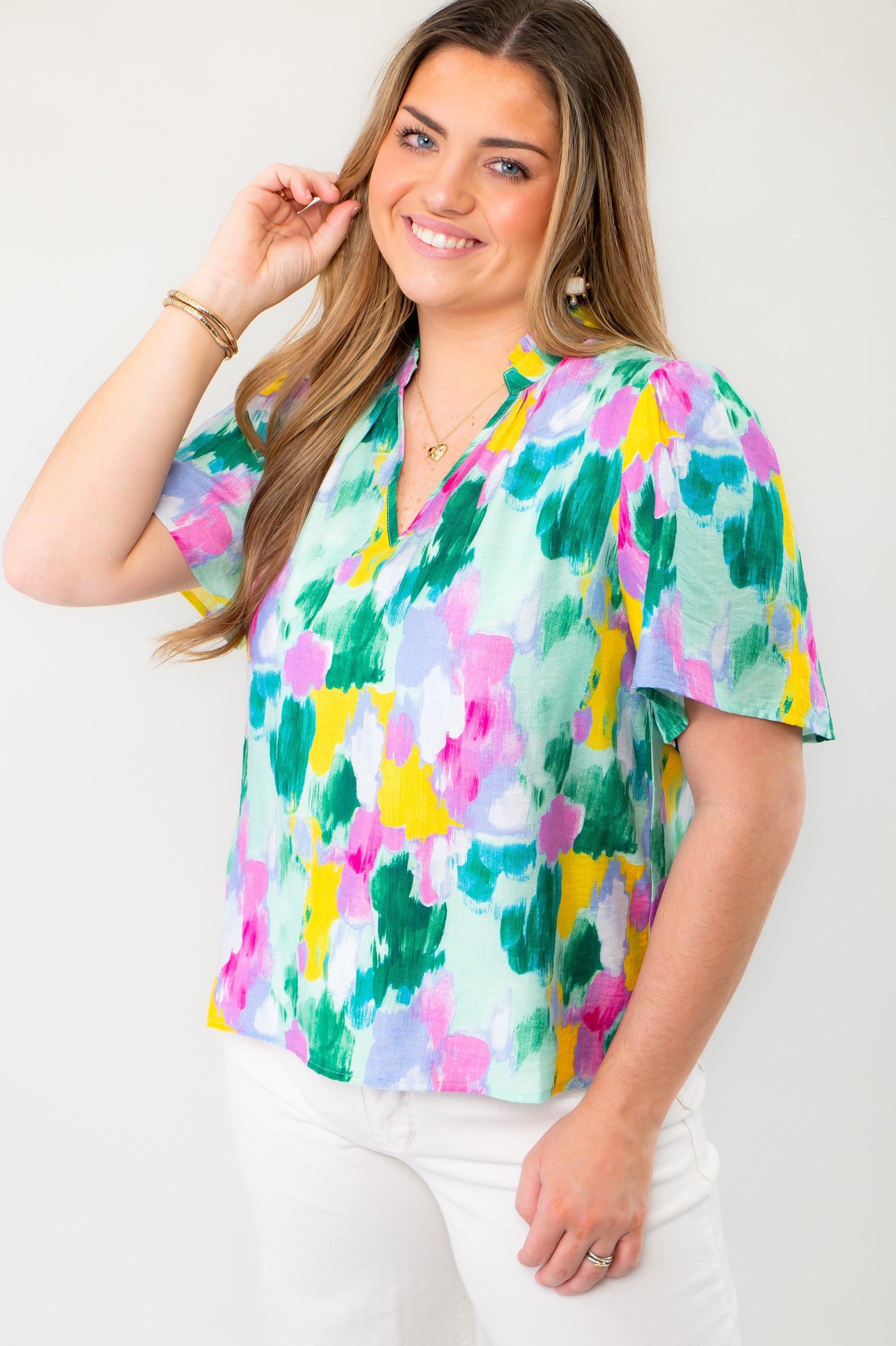 Model wearing THML Aqua Abstract Blouse with short sleeves and a relaxed fit, styled with white pants for a fresh spring outfit.