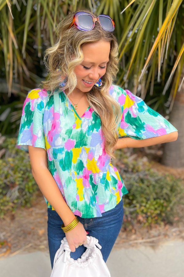 THML Aqua Abstract Blouse with vibrant brushstroke print, short sleeves, and v-neck. Perfect for spring and summer styling with jeans or skirts.