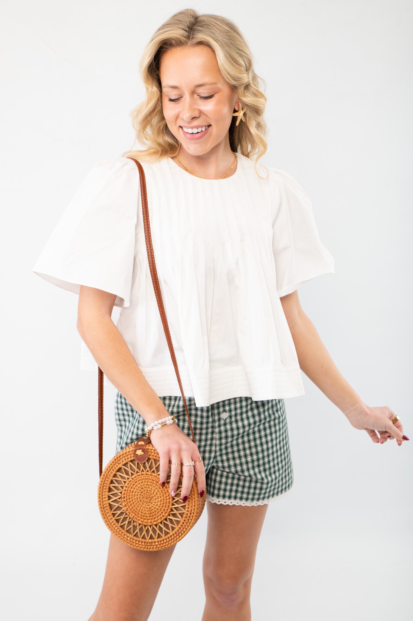 In This Moment Ivory Pleated Blouse with short sleeves and a crew neckline, paired with gingham shorts for a chic summer look.