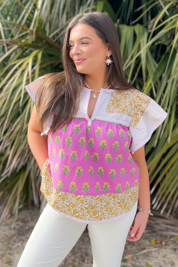 Outdoor shot of the Wildflower Pink &amp; Mustard Printed Ruffle Sleeve Top, styled with white pants for a fresh and fashionable spring ensemble.