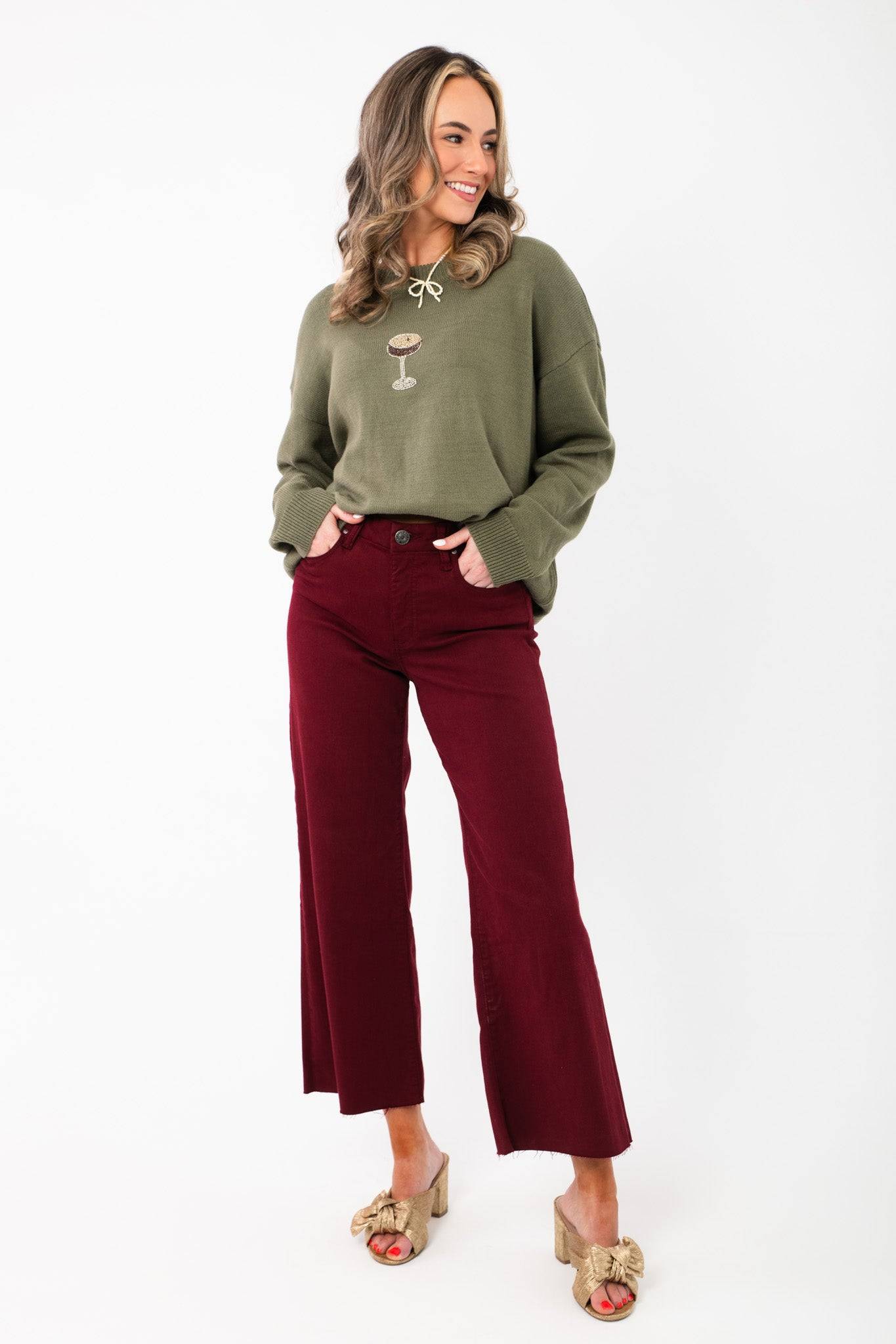 Model wearing Kut Maroon Meg High Rise Jeans with wide leg silhouette and raw hem. Ideal for holiday styling with heels or boots.