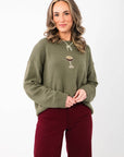 Front view of the Martini A Day Olive Beaded Sweater featuring a beaded espresso martini glass, paired with burgundy pants for a festive look.