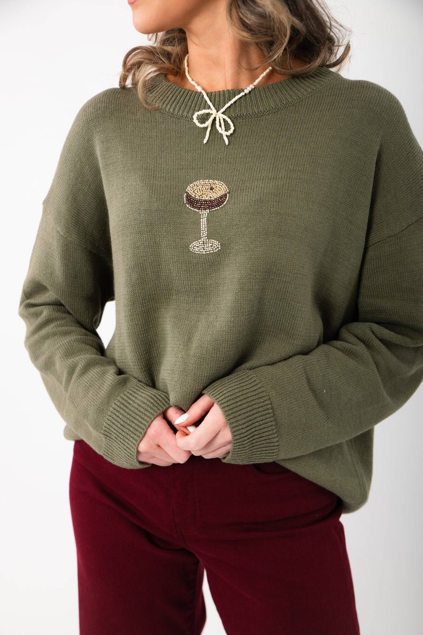 Close-up of the Martini A Day Olive Beaded Sweater showcasing detailed espresso martini beadwork on soft olive knit fabric. Ideal for trendy winter wear.