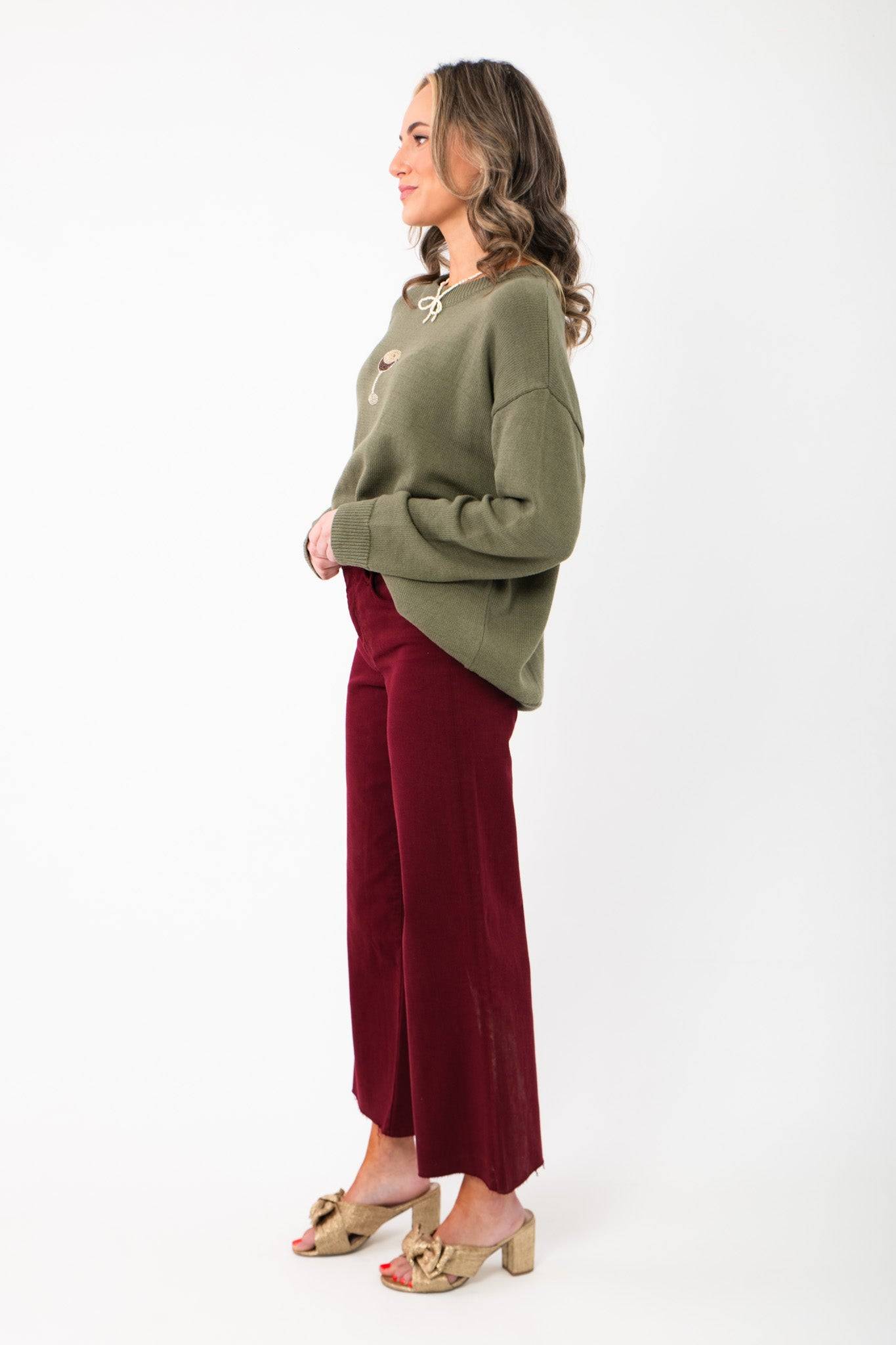 Side view of Kut Maroon Meg High Rise Wide Leg Jeans showing relaxed fit and cropped length. Styled with a cozy green sweater.