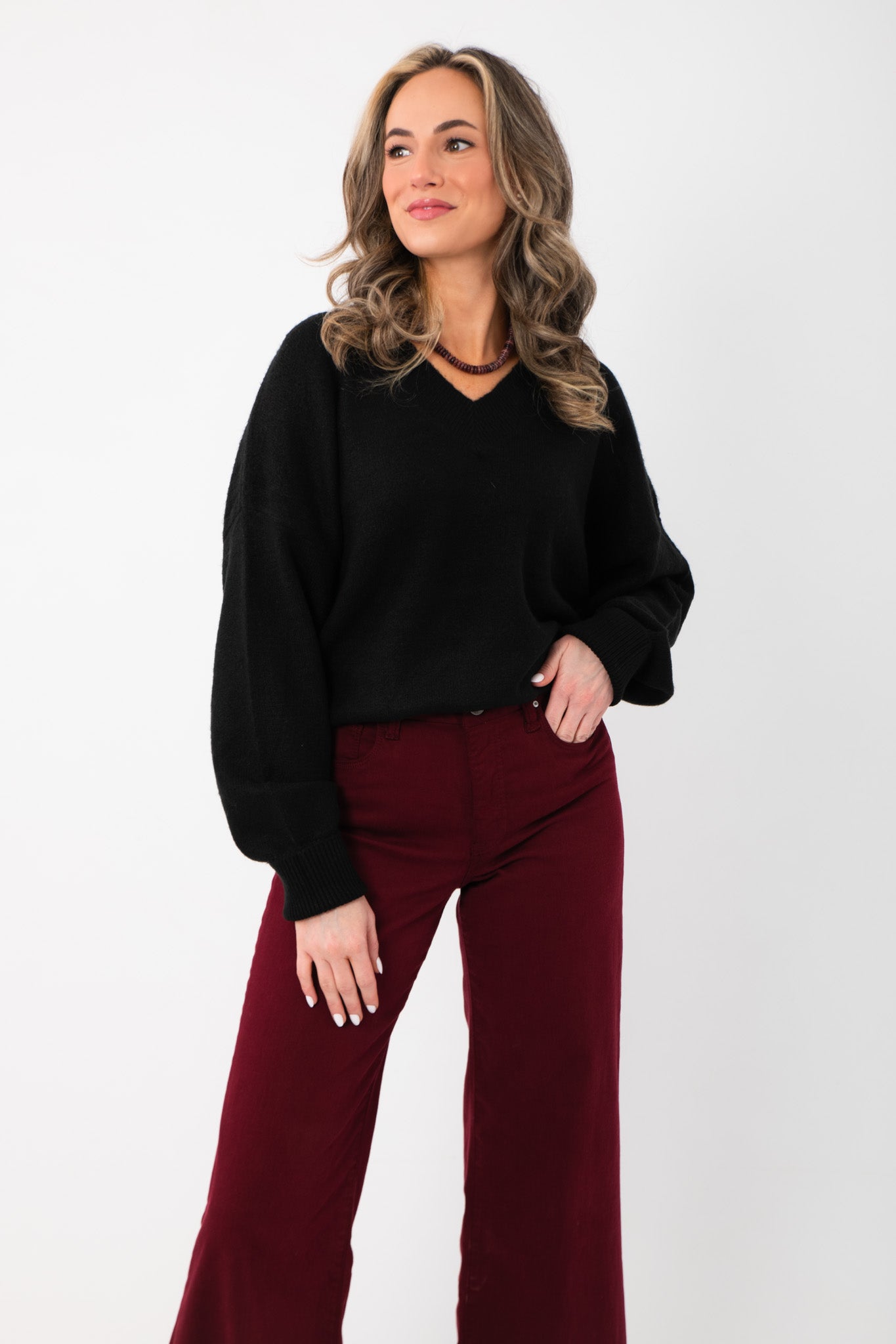 Olivia Oversized Black V‑Neck Sweater with relaxed fit and long sleeves, styled with burgundy pants for a cozy boutique knit look.