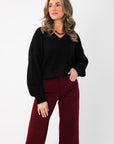 Olivia Oversized Black V‑Neck Sweater with relaxed fit and long sleeves, styled with burgundy pants for a cozy boutique knit look.