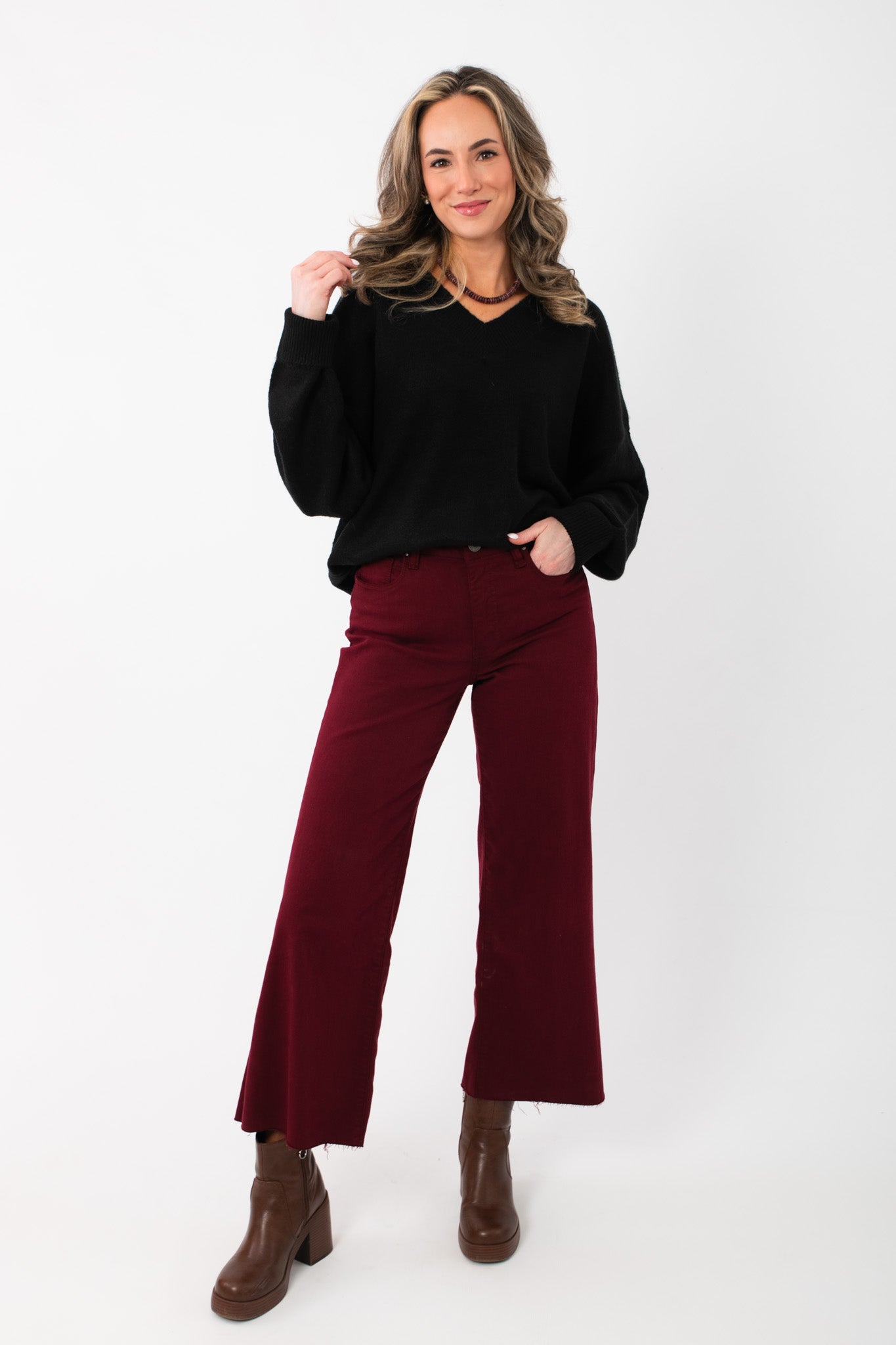 Women's Olivia Oversized Black V‑Neck Sweater paired with wide-leg burgundy trousers and brown boots, ideal for casual or dressy wear.