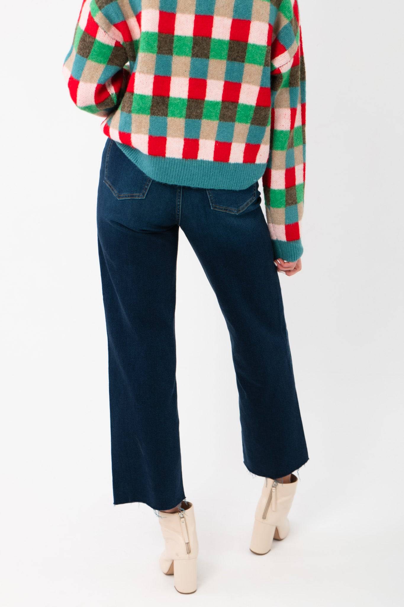 Close-up of the lower back of the Holiday Check Knit Sweater and dark denim jeans, highlighting the sweater’s festive check pattern.