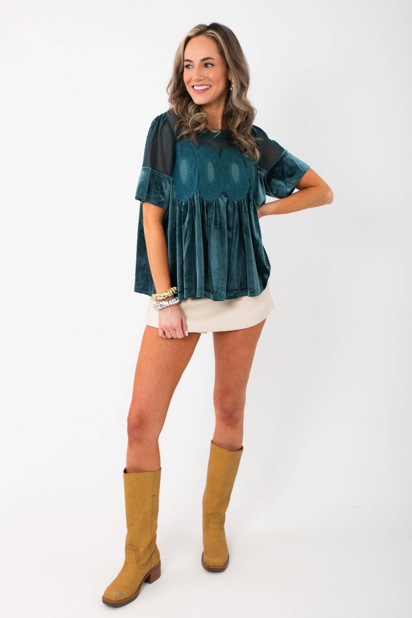 Model wearing Lacy Teal Velvet Babydoll Top with tan boots and cream skirt, showcasing festive lace and velvet design for winter fashion.